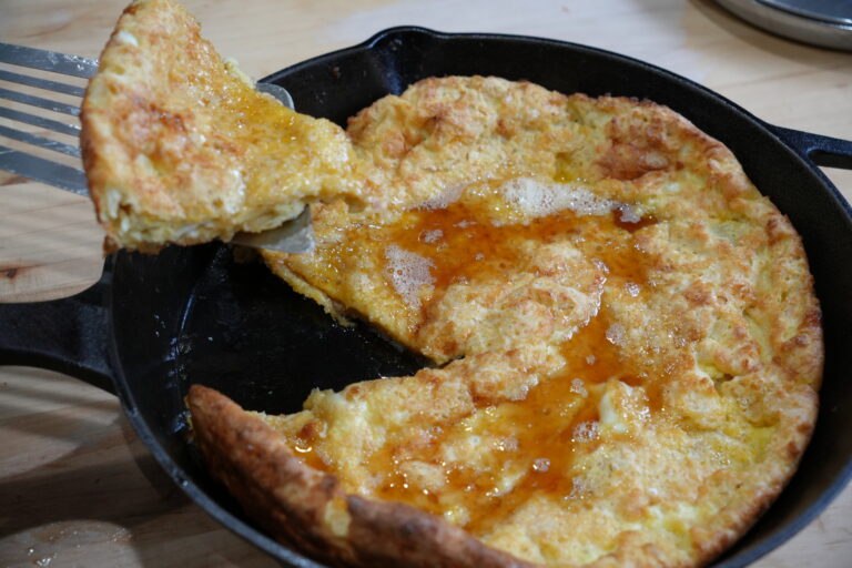 German Pancakes drizzled with maple syrup being cut into and the slice is being taken out of the cast iron pan.