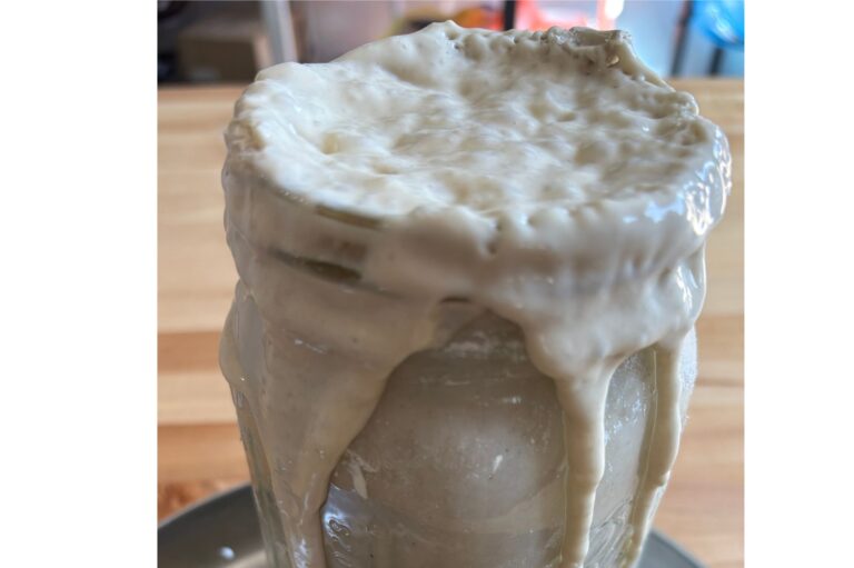 Bubbly sourdough starter in a glass jar that is overflowing