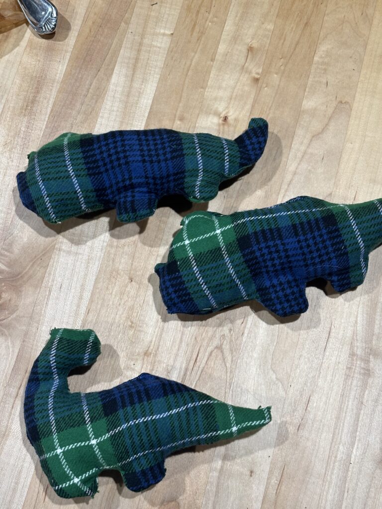 three DIY handmade stuffed animal dinosaurs with green and blue fabric. two are triceratops and one is a long neck.