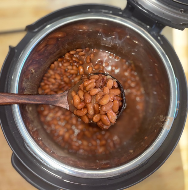 Homemade pinto beans fresh out of the pressure cooker, scooped in a wooden scooper.