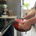 woman holding red dutch oven pan and placing it in oven