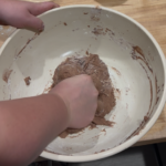 Chocolate sourdough in a bowl being kneaded by hand