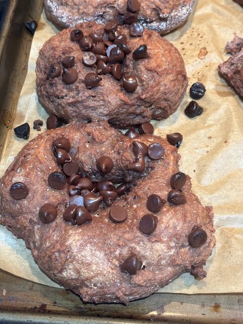 3 Chocolate Sourdough Bagels laying on parchment paper with chocolate chips on top of them