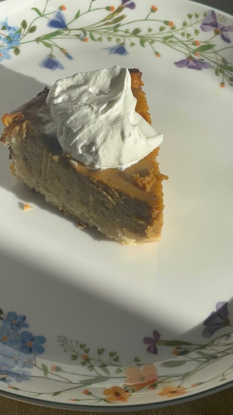 homemade pumpkin pie on a glass plate with flowers around it and a dollop of whipped cream on top.