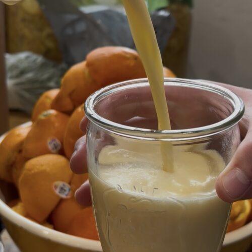 Picture of Orange Julius being poured into a glass with oranges in the background